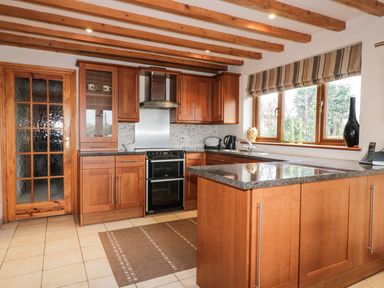 A kitchen with wooden cabinets a stove a window with striped blinds and a wooden door at Lynton House in Ruardean Hill near Drybrook
