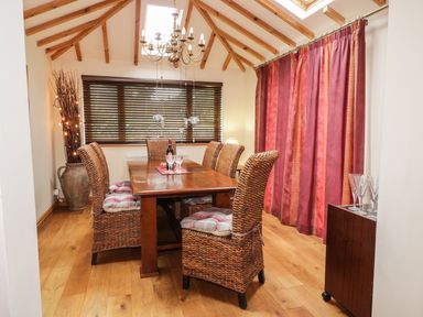 A dining room with wooden table and wicker chairs with cushions at Lynton House in Ruardean Hill near Drybrook