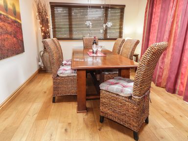 A dining room with a wooden table rattan chairs cushions and blinds at Lynton House in Ruardean Hill near Drybrook