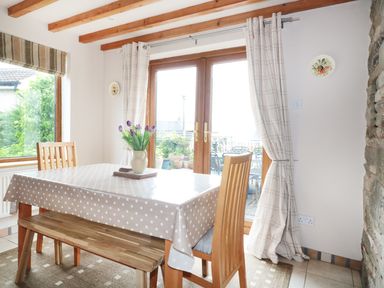 A dining area with a wooden table covered with a polka dot tablecloth and wooden chairs near glass doors at Lynton House Ruardean Hill near Drybrook