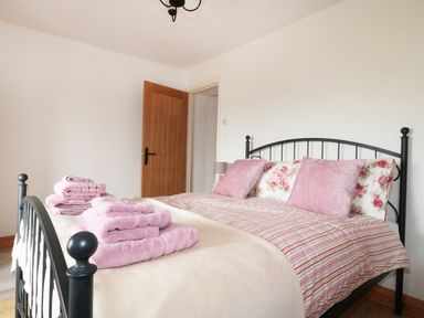 A bedroom with a black metal bed frame pink and floral pillows folded pink towels and an open wooden door at Lynton House in Ruardean Hill near Drybrook
