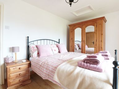 A bedroom with a double bed pink pillows wooden wardrobe and bedside table at Lynton House in Ruardean Hill near Drybrook