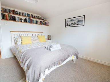 A bedroom with a bed yellow pillows folded towels on the bed a bookshelf on the wall and a framed picture at Lynton House in Ruardean Hill near Drybrook