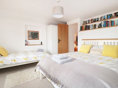 A bedroom with two beds yellow pillows books on wall shelves and a wooden door at Lynton House Ruardean Hill near Drybrook