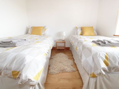 A bedroom with two single beds a wooden side table with lamp and a small rug on wooden floor at Lynton House in Ruardean Hill near Drybrook