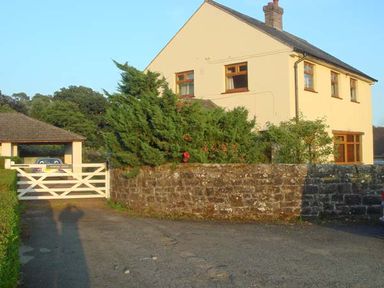 An outdoor view of a two-story house with a stone wall and shrubs nearby at Hartam House in Falstone near Kielder and Bellingham