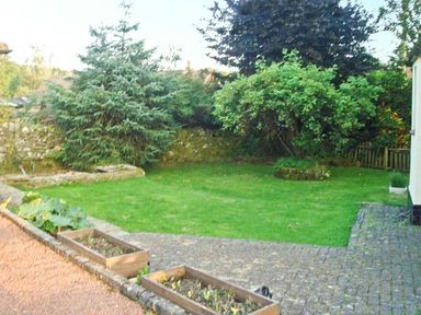 A garden area with grass lawn trees shrubs flowerbeds and a paved path at Hartam House in Falstone near Kielder and Bellingham