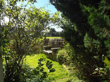 A garden with grass trees shrubs and a stone wall with a wooden gate at Hartam House in Falstone near Kielder and Bellingham