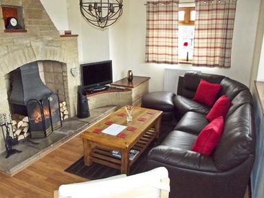 A living room with a stone fireplace a leather sofa with red cushions a wooden coffee table and a television at Hartam House in Falstone near Kielder and Bellingham
