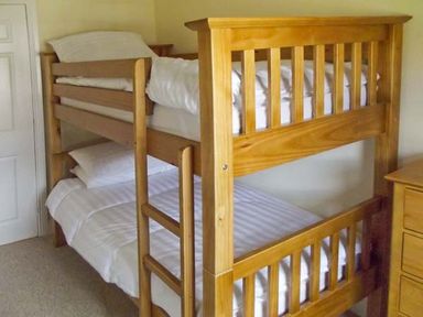 A wooden bunk bed with white bedding in a bedroom
