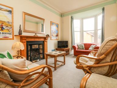A living room with a fireplace chairs a sofa a coffee table and a television at Penryn in Ilfracombe