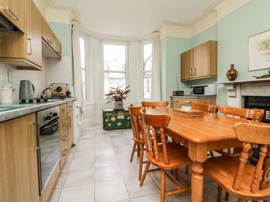 A kitchen with wooden dining table and chairs near windows and cabinets at Penryn in Ilfracombe