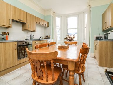 A kitchen with wooden cabinets a wooden dining table and chairs and large windows at Penryn in Ilfracombe