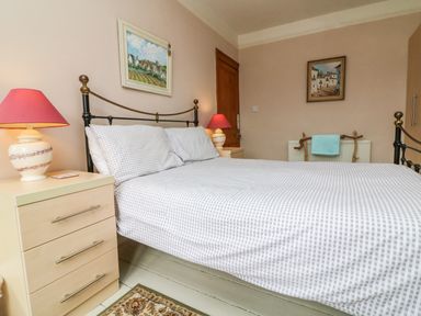 A bedroom with a bed with checkered bedding two bedside tables with lamps a wooden door two paintings and a towel on a rack at Penryn in Ilfracombe