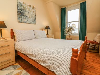A bedroom with a wooden bed a plant by the window and bedside tables with lamps at Penryn in Ilfracombe
