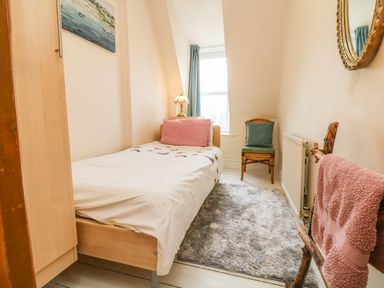 A small bedroom with a single bed a pink pillow a wooden chair a rug and a towel rack at Penryn in Ilfracombe
