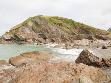 Rocky shoreline with a hill covered in grass and a stone wall near the water at Penryn in Ilfracombe