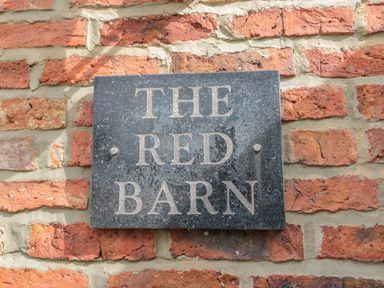 A black stone plaque with the words The Red Barn mounted on a red brick wall at The Red Barn in Longframlington near Alnwick