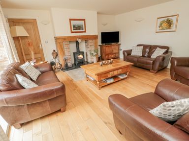 A living room with brown leather sofas a wooden coffee table a fireplace and a television at The Red Barn in Longframlington near Alnwick