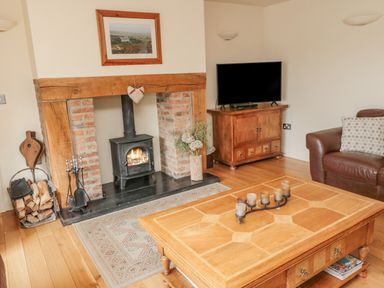 A living room with a fireplace a wood stove a wooden coffee table and a television at The Red Barn in Longframlington near Alnwick