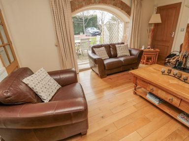 A living room with two brown leather sofas a wooden coffee table and a large arched window at The Red Barn in Longframlington near Alnwick