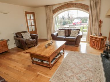 A living room with brown leather sofas wooden coffee table and large window at The Red Barn in Longframlington near Alnwick