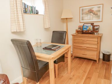 A small room with a wooden table and two leather chairs a wooden chest of drawers with books a floor lamp and a window with curtains at The Red Barn in Longframlington near Alnwick