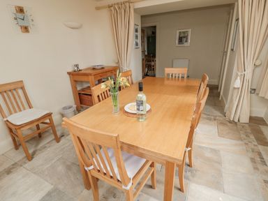 A dining room with a wooden table and chairs a bottle and flowers on the table and curtains at The Red Barn Longframlington near Alnwick