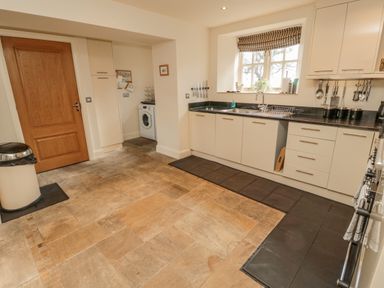 A kitchen with white cabinets a washing machine under a counter a wooden door and a window with striped blind at The Red Barn in Longframlington near Alnwick