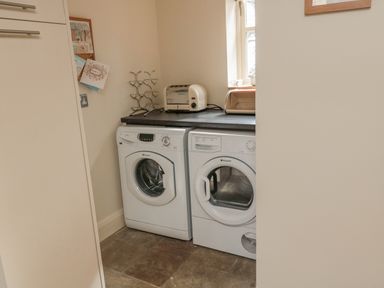 A laundry room with a washing machine and dryer under a countertop with a toaster and breadbox at The Red Barn in Longframlington near Alnwick
