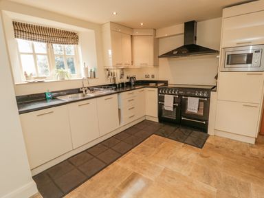 A kitchen with cream cabinets black countertops a black stove a microwave and a window with a striped blind at The Red Barn in Longframlington near Alnwick