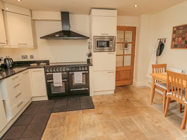 A kitchen with a black stove and oven a microwave above a wood door and a small dining table with two chairs at The Red Barn in Longframlington near Alnwick