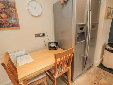 A kitchen area with a wooden table and two chairs a silver refrigerator a small black radio clock on the wall at The Red Barn in Longframlington near Alnwick