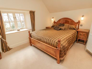 A bedroom with a wooden bed striped bedding two bedside tables and a window with curtains at The Red Barn in Longframlington near Alnwick
