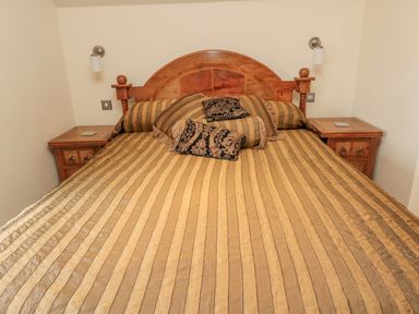 A bedroom with a wooden bed with striped bedspread and two side tables with lights at The Red Barn in Longframlington near Alnwick