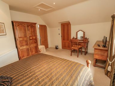 A bedroom with a bed a wooden wardrobe a dressing table a chair and a wooden desk with a TV at The Red Barn in Longframlington near Alnwick