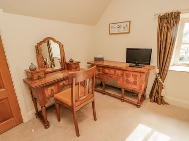 A room with wooden desk and mirror, wooden chair, wooden cabinet with TV and window with curtain at The Red Barn in Longframlington near Alnwick