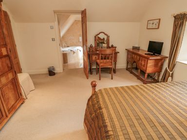 A bedroom with a bed a dressing table a television on a cabinet and a doorway leading to a bathroom at The Red Barn in Longframlington near Alnwick
