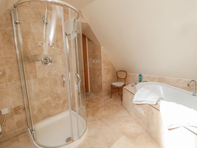 A bathroom with a glass shower enclosure a bathtub a wooden chair and beige tiled walls and floor at The Red Barn in Longframlington near Alnwick