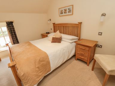 A bedroom with a wooden bed and side tables a beige blanket and cushions and a chair at The Red Barn in Longframlington near Alnwick