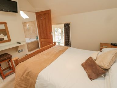 A bedroom with a wooden bed and pillows next to a window and an en suite bathroom at The Red Barn in Longframlington near Alnwick