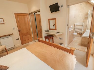 A bedroom with a bed a wooden door a wall-mounted television a dressing table and a bathroom at The Red Barn in Longframlington near Alnwick
