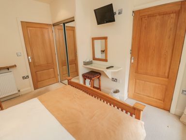 A bedroom with a bed a wall mounted TV a dressing table with a stool and two wooden doors at The Red Barn in Longframlington near Alnwick