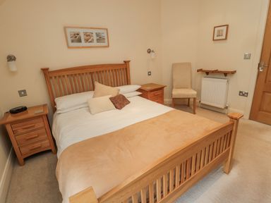A bedroom with a wooden bed and bedside tables a chair and framed pictures on the walls at The Red Barn in Longframlington near Alnwick