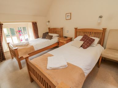 A bedroom with two single wooden beds a window with curtains and a small wooden bedside table at The Red Barn in Longframlington near Alnwick