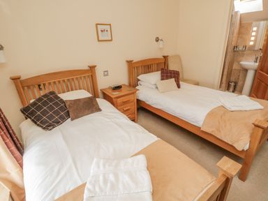 A bedroom with two single wooden beds a bedside table and an en suite bathroom at The Red Barn in Longframlington near Alnwick