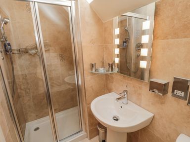 A bathroom with a shower cubicle a sink a mirror with lights and wall-mounted accessories at The Red Barn in Longframlington near Alnwick