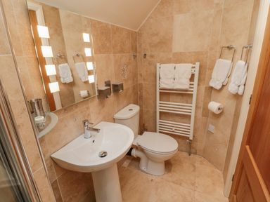 A bathroom with a pedestal sink a toilet a mirror with lights and towels on racks at The Red Barn Longframlington near Alnwick