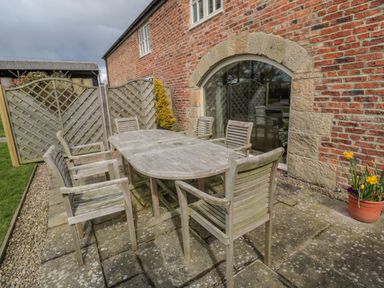 An outdoor patio with wooden table and six chairs next to a brick building with an arched window at The Red Barn in Longframlington near Alnwick