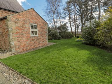 A garden with grass and bushes beside a brick house at The Red Barn in Longframlington near Alnwick